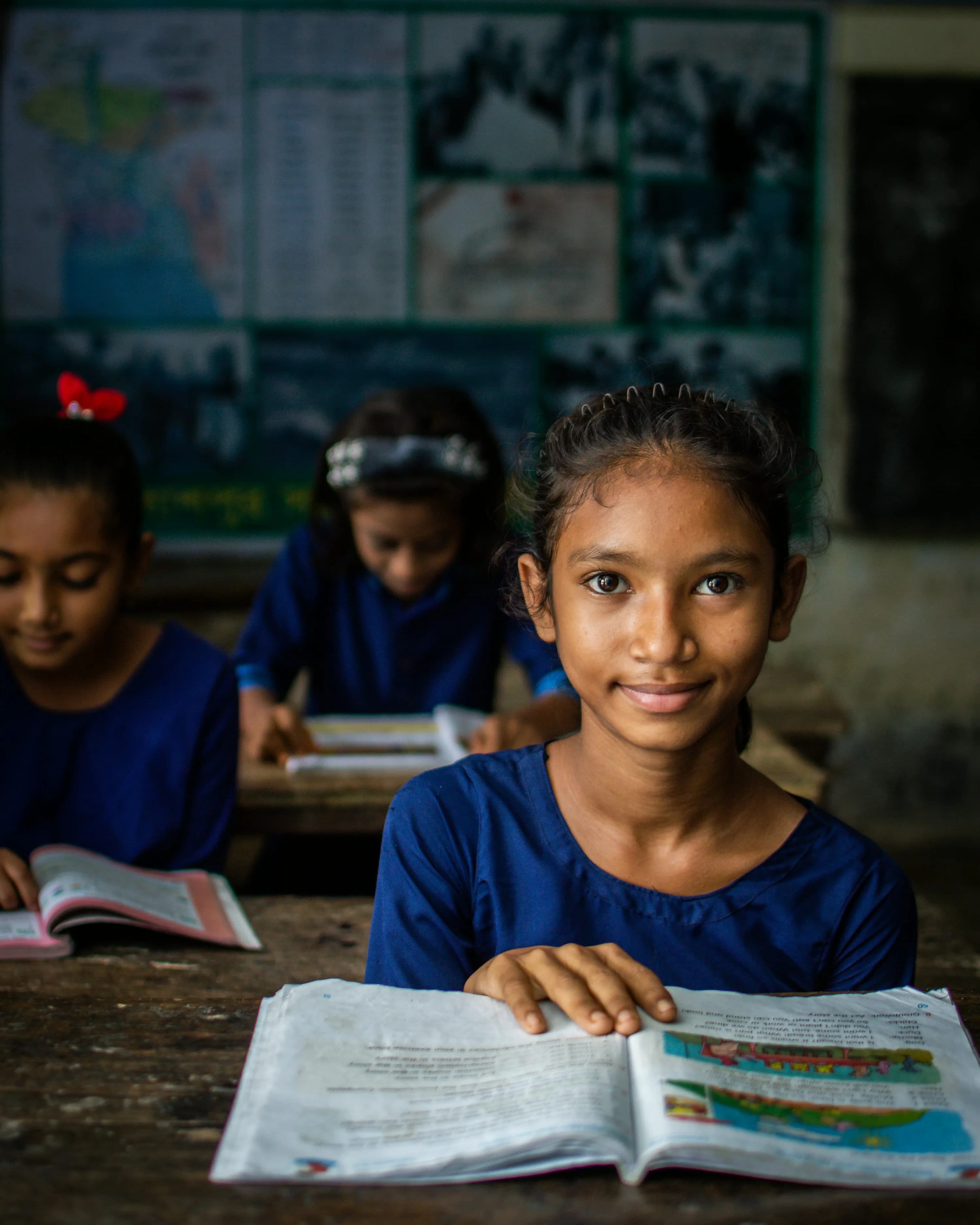 A schoolgirl supported by Shri Shivshakti Vidhyapeeth looks up from her textbook in class.